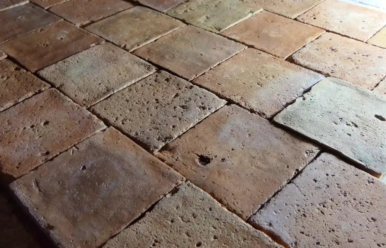 Gros plan sur un sol en tomette ancienne, aux carreaux carrés en terre cuite aux nuances chaudes et irrégulières, témoignant du passage du temps.
