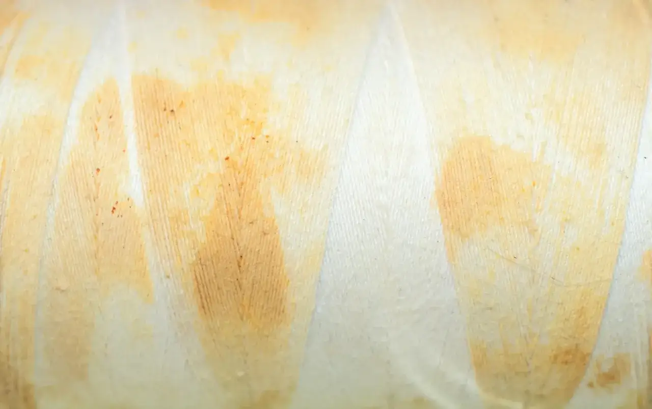 Gros plan sur un fil blanc avec une tache jaune, comme si un v&ecirc;tement blanc avait &eacute;t&eacute; tach&eacute; par du th&eacute; ou du caf&eacute;.