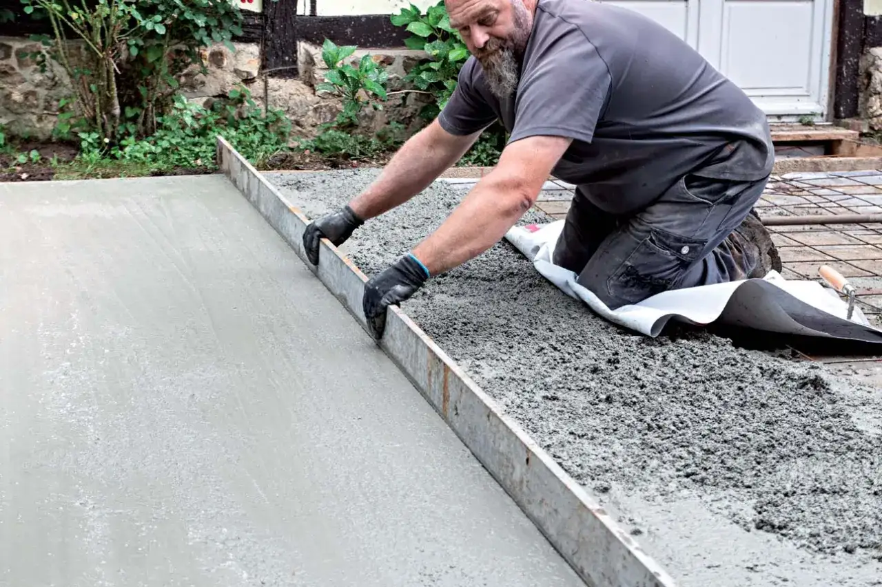 Un homme lisse une dalle de b&eacute;ton fra&icirc;chement coul&eacute;e, pos&eacute;e sur une b&acirc;che. La question 