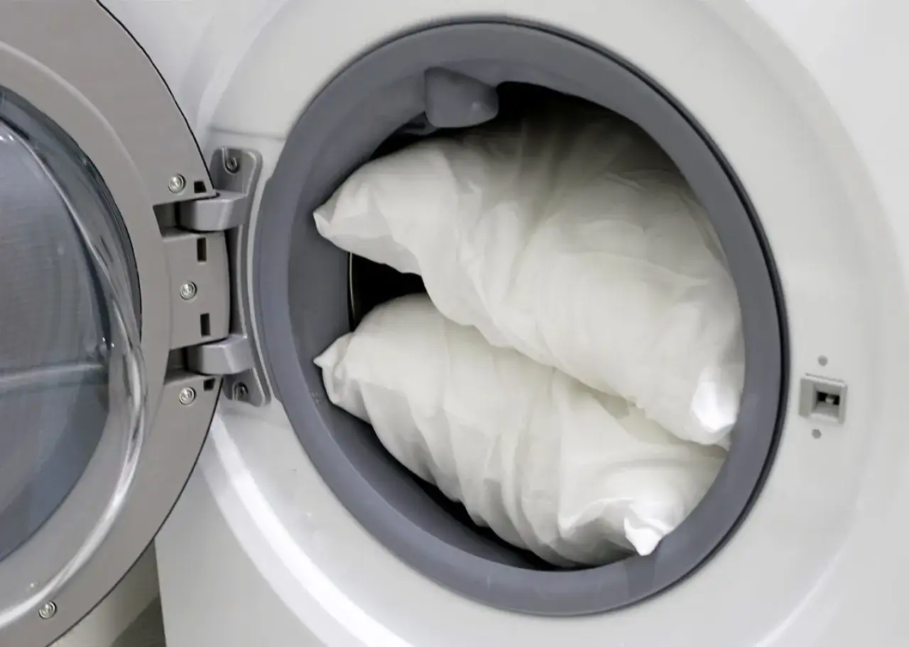 Deux oreillers blancs sont pr&ecirc;ts pour le nettoyage dans le tambour d'une machine &agrave; laver.