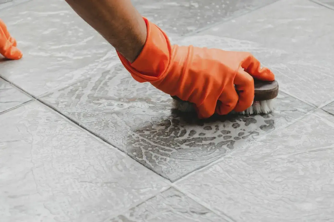 Main tenant, gant&eacute;, frotte le sol carrel&eacute; avec une brosse pour nettoyer le ciment sec.