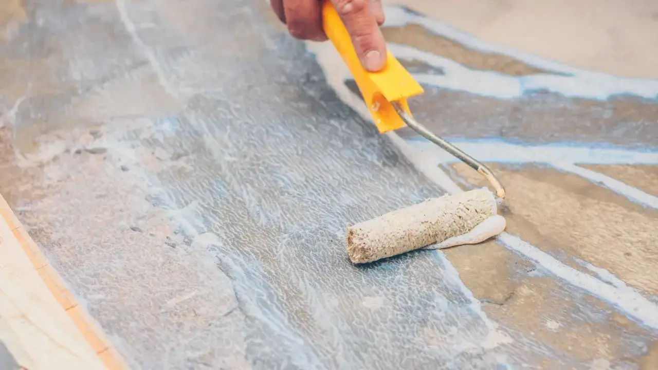 Application d'un primaire d'accrochage pour fa&iuml;ence avec un rouleau. Le produit blanc est &eacute;tal&eacute; sur une surface grise et textur&eacute;e.