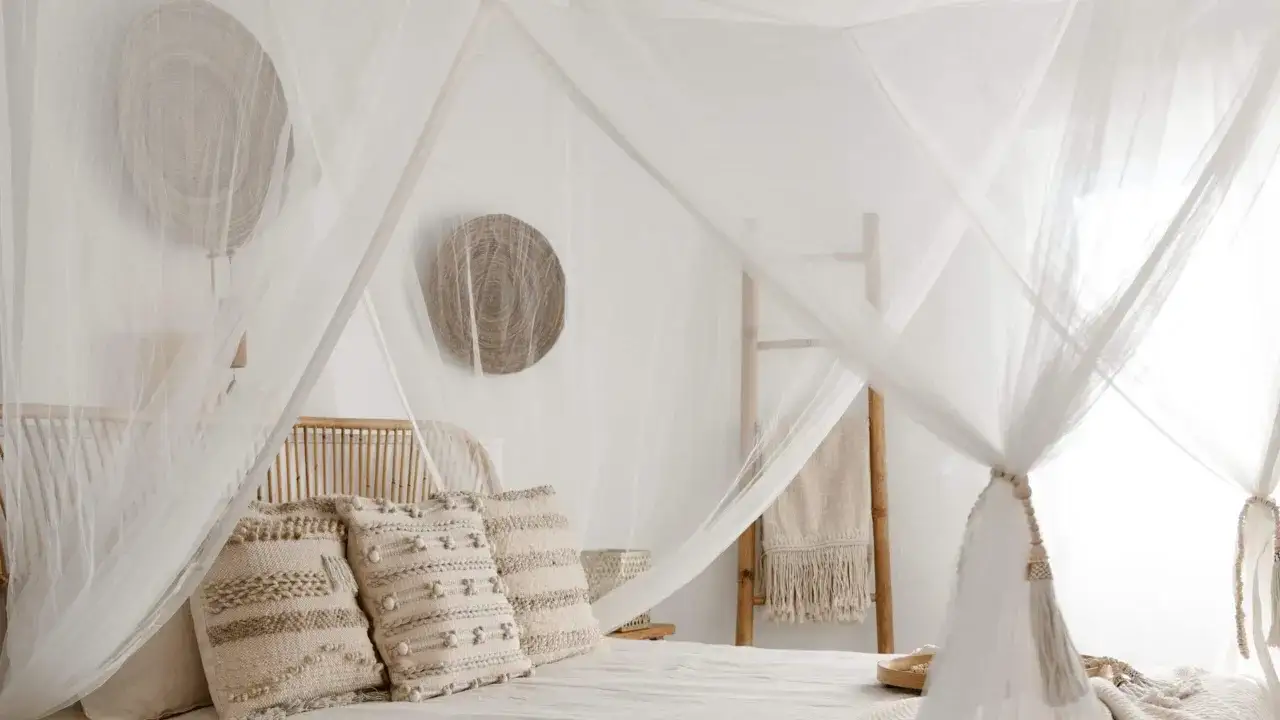 Lit douillet sous moustiquaire, une solution naturelle pour éloigner les moustiques la nuit. Décoration bohème avec coussins texturés et paniers en osier.