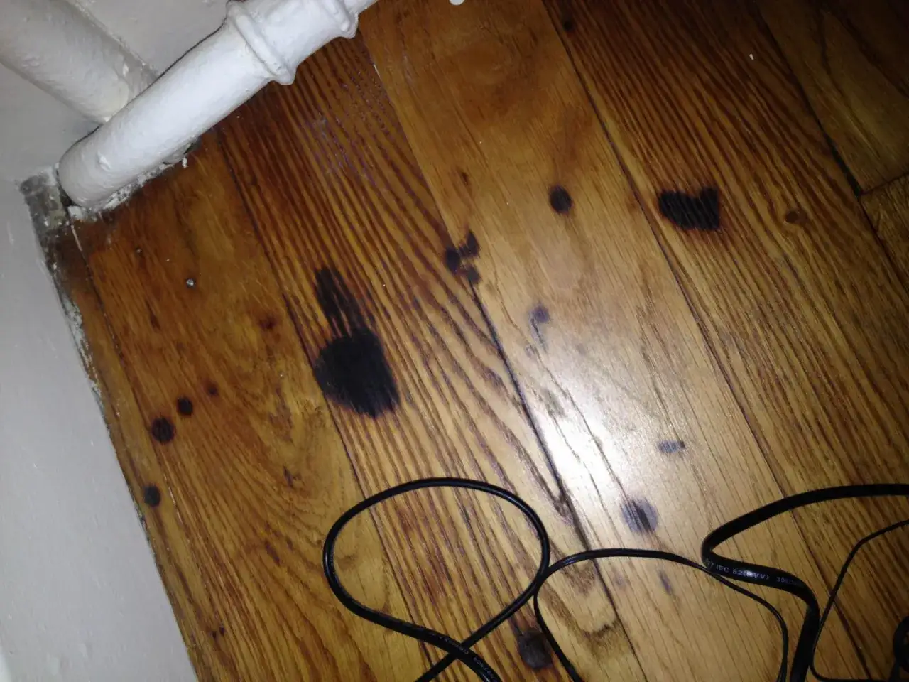 Parquet vitrifi&eacute; avec des traces sombres, peut-&ecirc;tre des marques de frottement &agrave; enlever. Des c&acirc;bles noirs sont pos&eacute;s au sol.