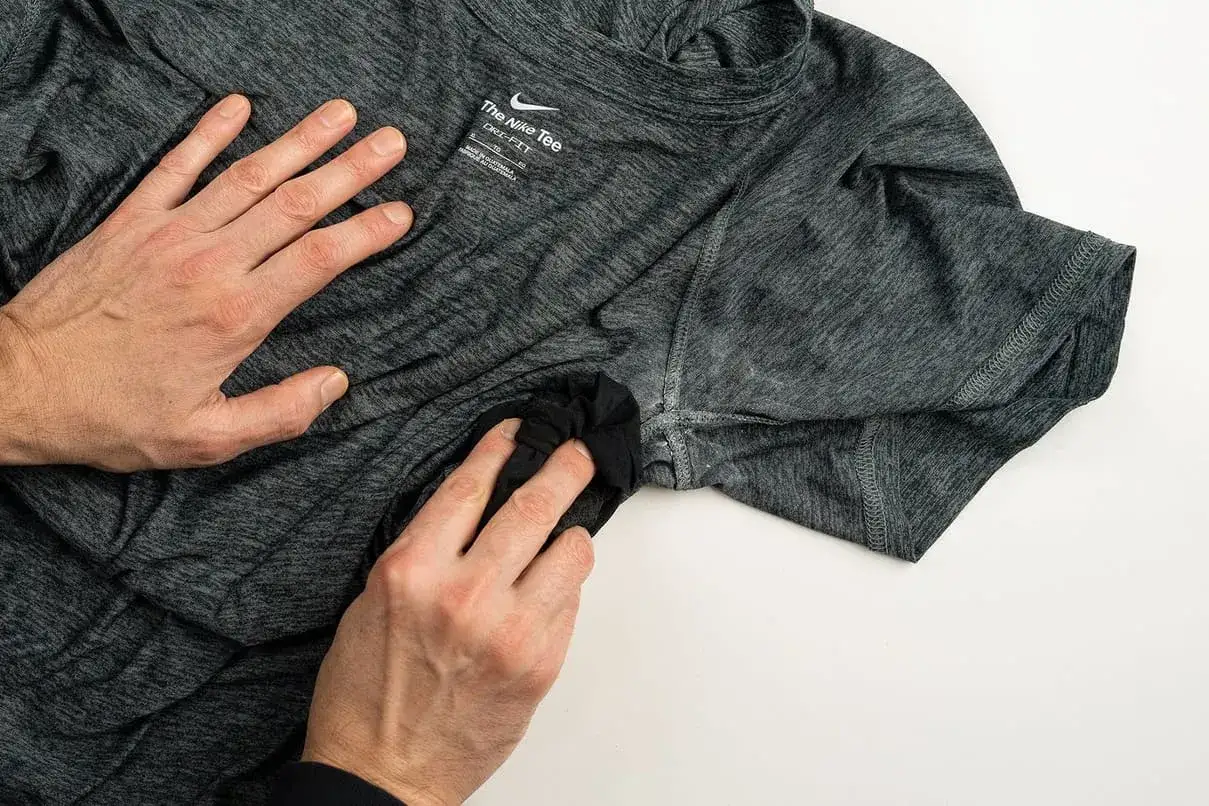 Main d'homme frottant une tache sous l'aisselle d'un t-shirt gris Nike. Astuce pour comment enlever les taches sous les aisselles.
