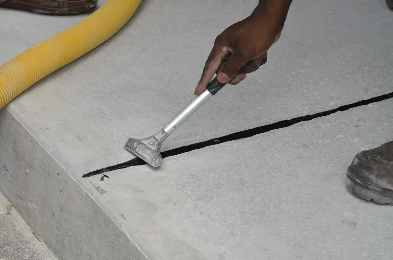 Maintenant, on peut couler une dalle en plusieurs fois. Un ouvrier applique un produit noir dans une jointure de béton avec un grattoir.