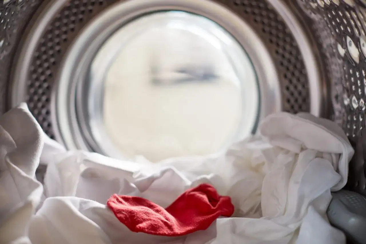 Vue de l'int&eacute;rieur d'une machine &agrave; laver avec du linge blanc et une chaussette rouge. Le bicarbonate de soude est id&eacute;al pour le linge couleur.