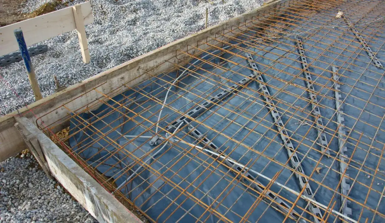 Préparation pour comment faire une dalle de terrasse : coffrage en bois, film plastique, et treillis métallique rouillé prêt à être coulé.