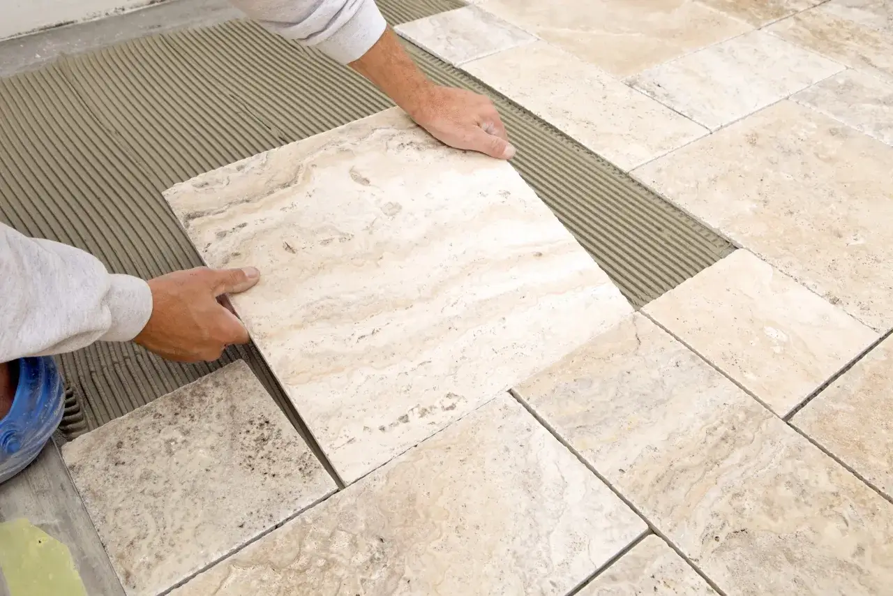 Pose de carreaux de travertin sur un lit de mortier. Les mains d'un poseur ajustent une nouvelle pierre.