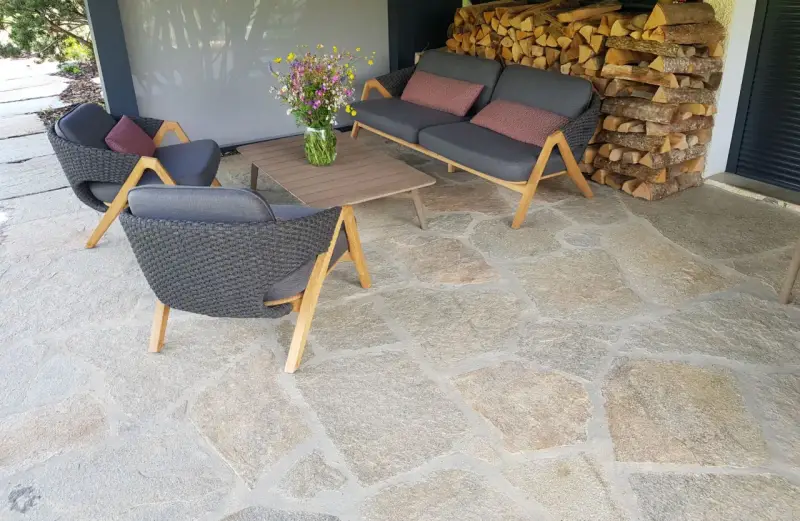 Terrasse en pierre naturelle extérieure, protégée par un imperméabilisant, avec mobilier de jardin confortable et un bouquet de fleurs sauvages.