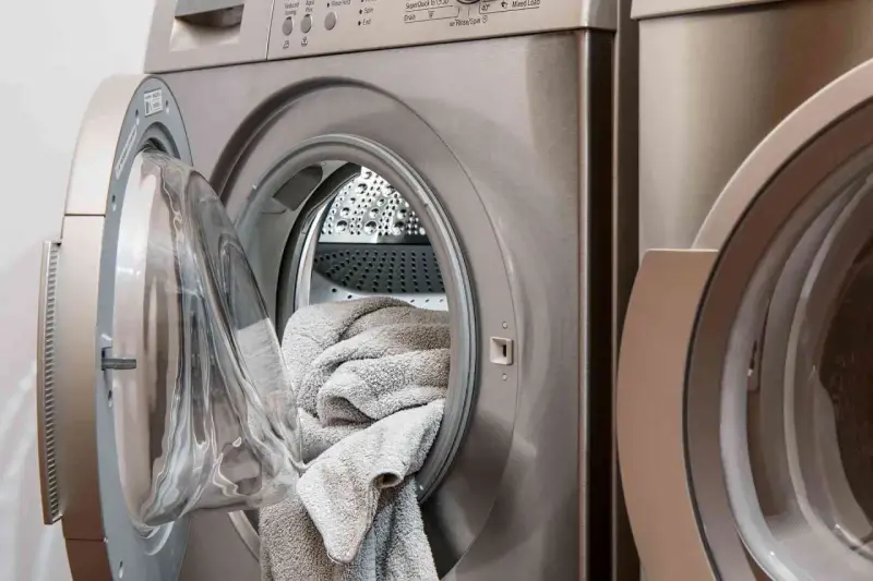 Machine à laver avec une porte ouverte, remplie de linge gris. Choisir la lessive la moins toxique pour un lavage sain.