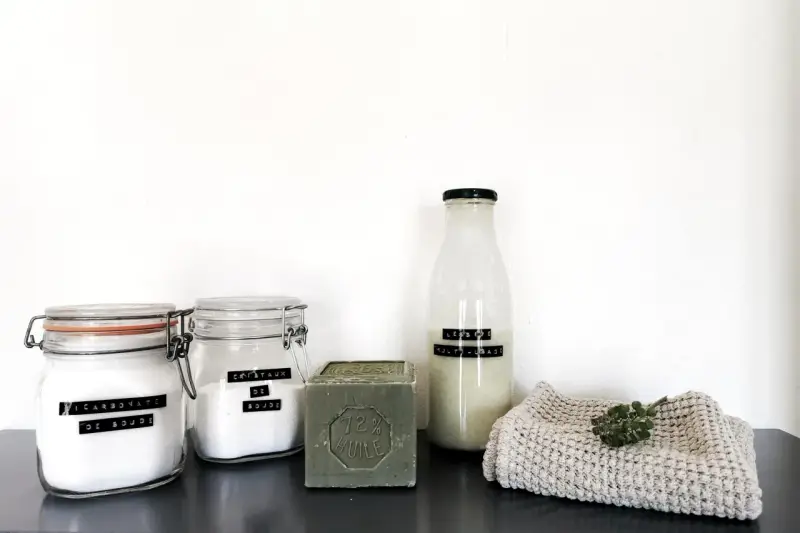 Ingrédients pour la meilleure recette lessive maison : bicarbonate de soude, cristaux de soude, savon de Marseille et une bouteille de lessive liquide.